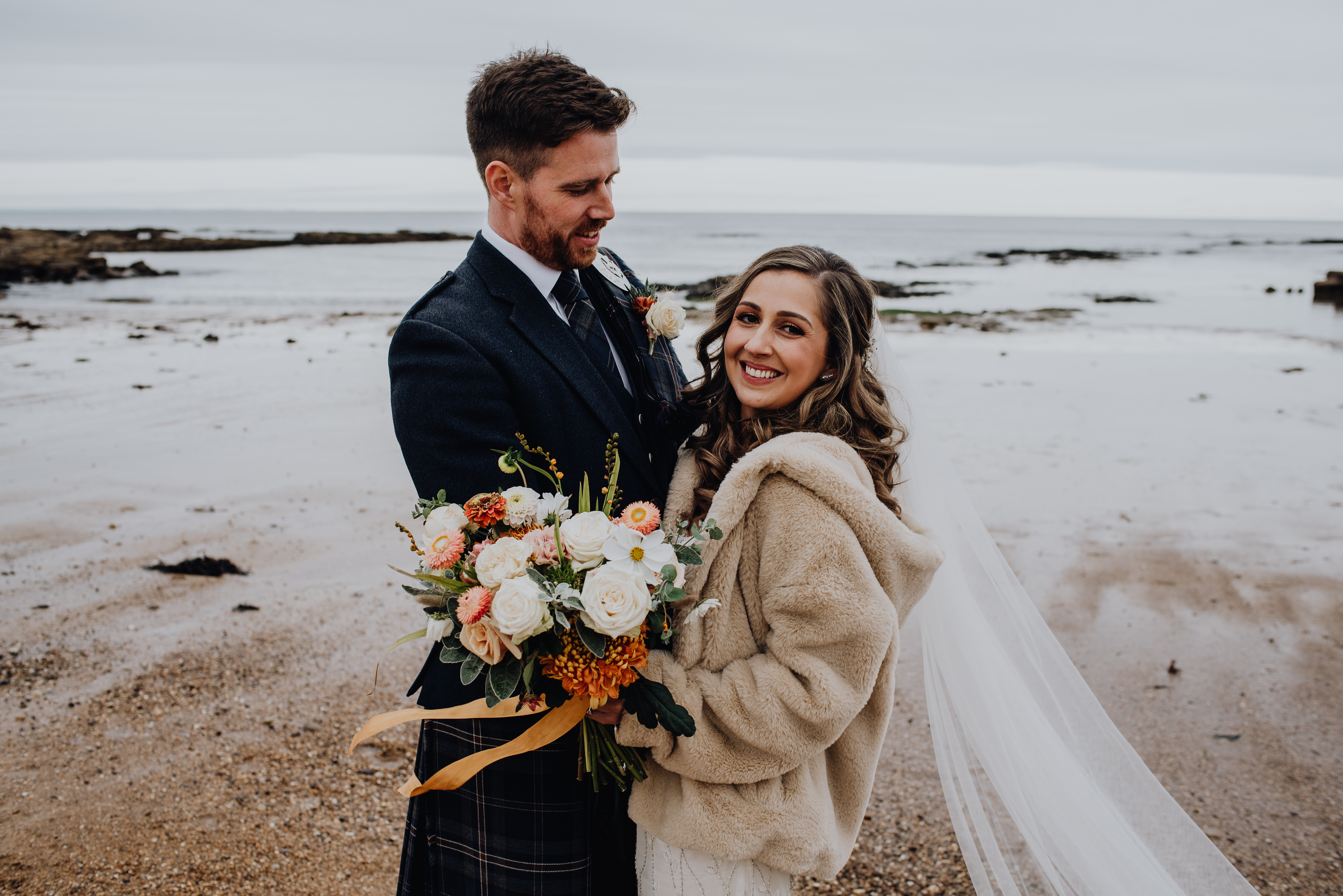 Couple on beach on wedding day with orange & cream bouquet
